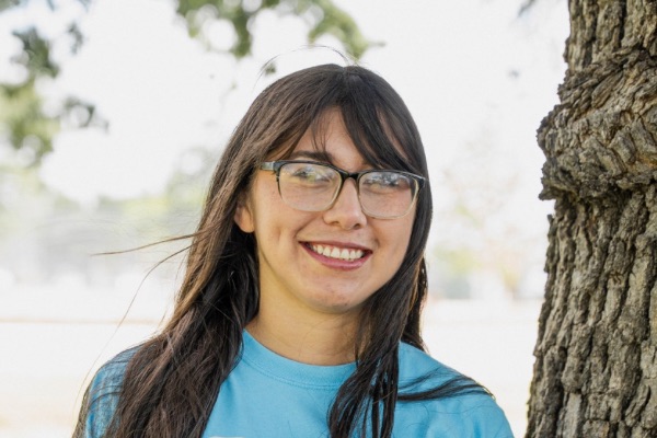 Teresa standing outside of Ark of Highland Lakes offices with turquoise ark logo t-shirt and a tree