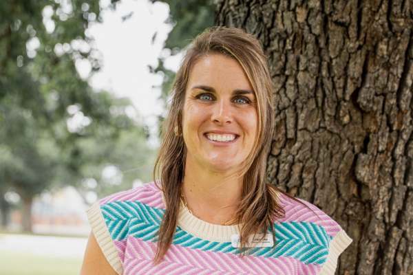Smiling woman in a colorful zigzag patterned top standing beside a tree in a park.
