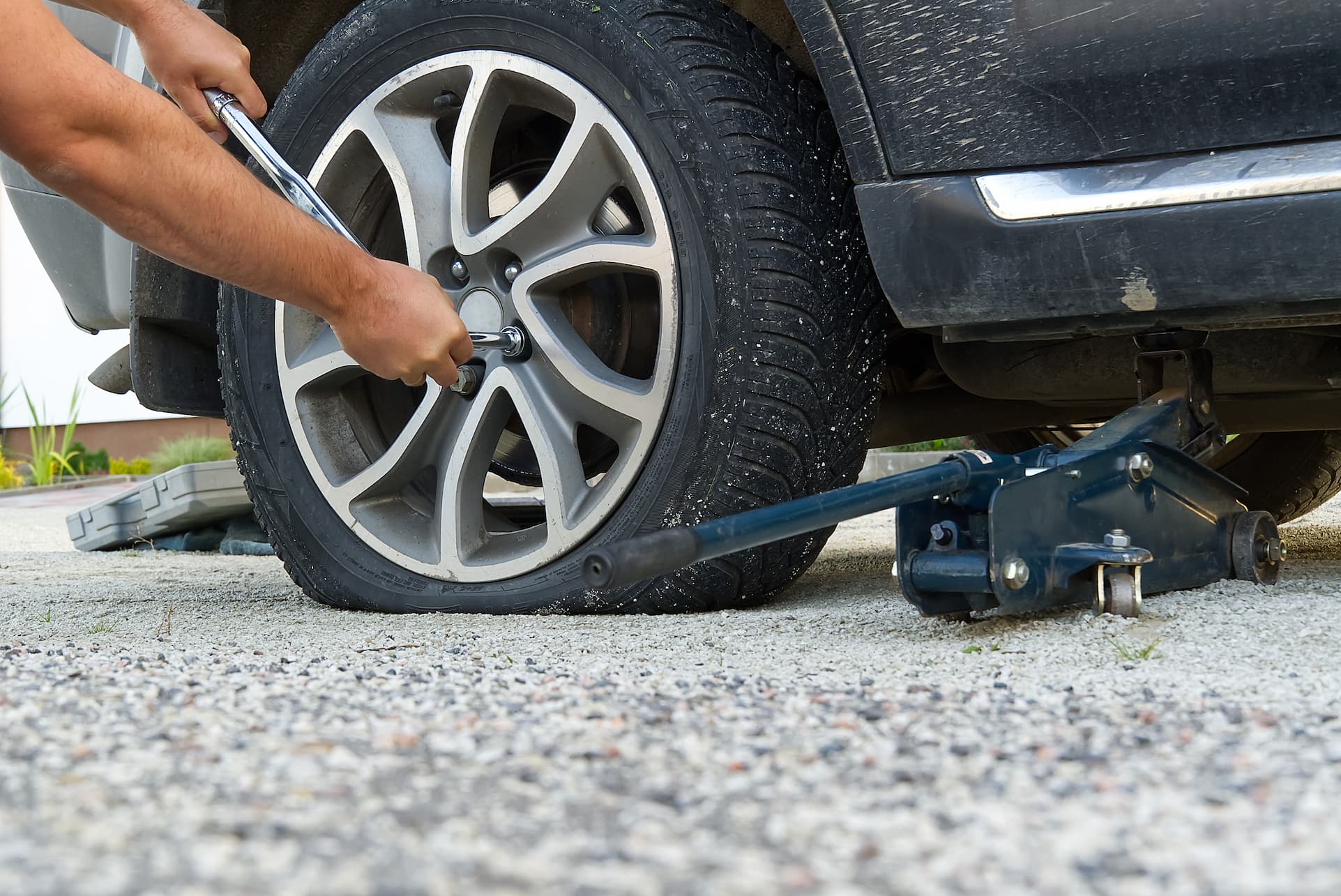Person uses a lug wrench to loosen lug nuts on a car wheel while the car is raised on a jack under the vehicle area